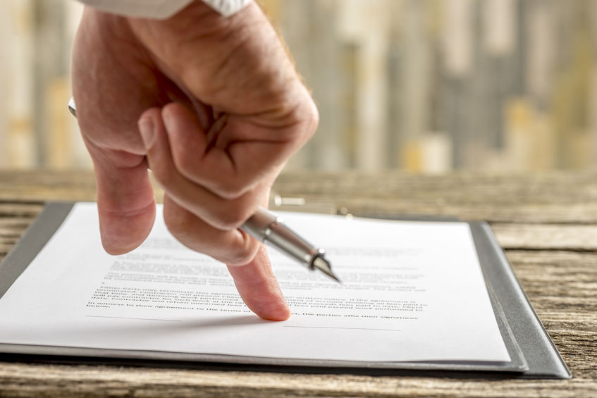 Closeup of male hand holding a pen pointing to a line at the end of a contract, document or application form ready for signature.