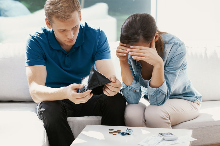 Newly married couple sitting at home looking at their finance problems in reference to a spouse being held liable for debt