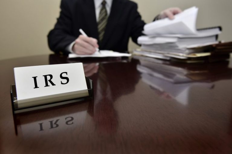 Image of IRS tax auditor man on wooden desk in reference to tax capital reporting requirements