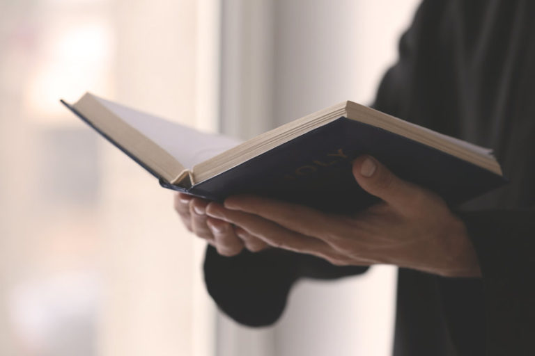 Young priest reading Bible indoors, closeup