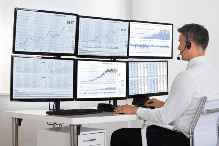 Side view of stock market broker looking at graphs on multiple screens in office