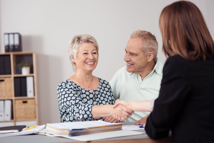 Happy Middle Aged Wife beside her Husband Shaking Hands to a Female Business Agent at the Table