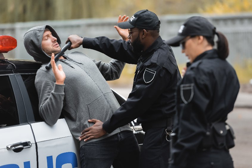 Picture of policeman with truncheon frisking offender with raised hands