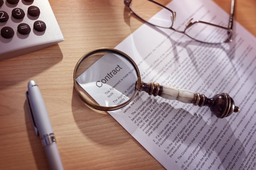 Picture of magnifying glass examining and signing a legal contract document